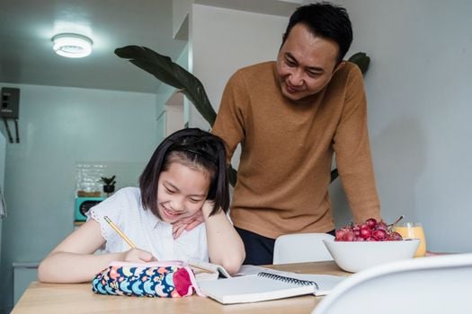 A father helps his daughter with homework in the kitchen, fostering learning and bonding.