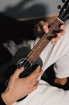 A musician's hands skillfully play the ukulele strings in a focused close-up shot.