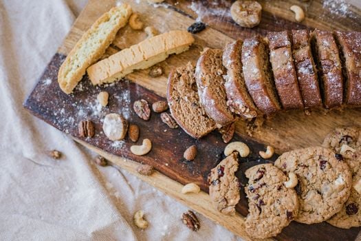A variety of baked goods including sliced bread, cookies, and nuts on a rustic wooden board.