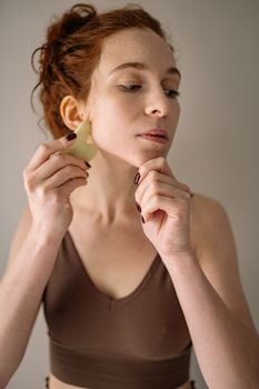 Woman practicing gua sha for face massage and self-care routine indoors.