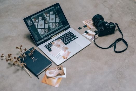 Top view of a creative workspace featuring a laptop, camera, and design materials, ideal for digital artists.