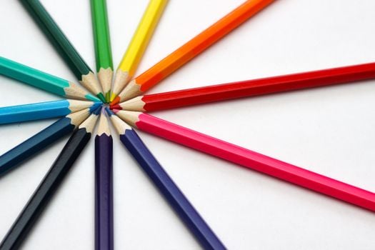 A close-up shot of colorful pencils arranged in a circular pattern on a white background, showcasing a variety of bright, vivid hues.