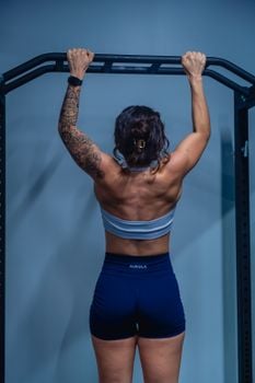 Back view of a strong woman performing pull-ups indoors, highlighting fitness and strength.