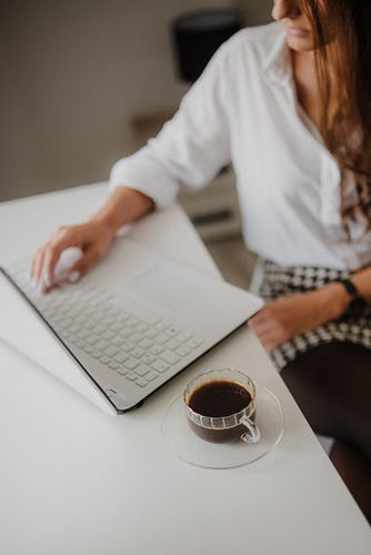 Close-up of a cup of coffee and woman working on a laptop in a blurry background.