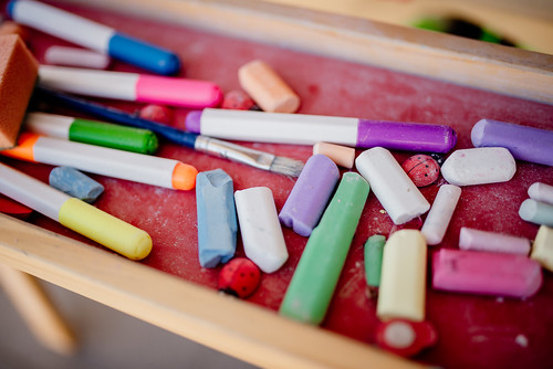 A variety of colorful chalk pieces and markers are scattered across a red art table