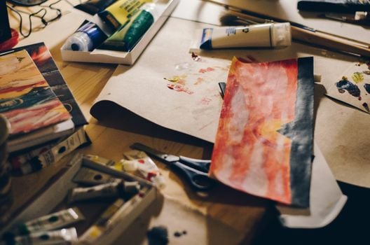 A close-up of art supplies and paintings on a wooden desk, showcasing vibrant creativity.