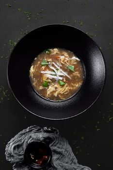 A top-down view of hot and sour soup garnished with greens in a black bowl.