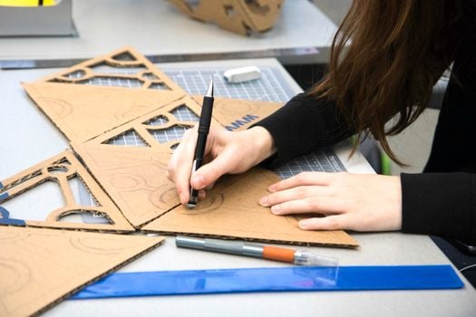 Close-up of a woman sketching architectural designs on cardboard at a desk.