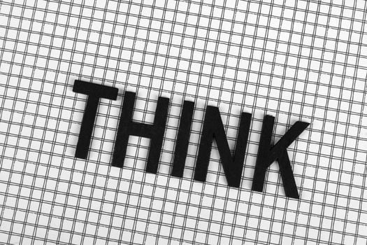 Black letters forming the word 'THINK' on a grid-like checkered background, emphasizing creativity.
