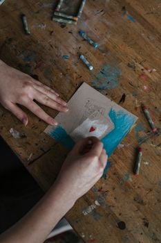 A person coloring a heart card with crayons on a wooden table, emphasizing creativity.