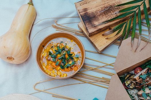 A cozy flat lay of a rustic table setting featuring a bowl of pumpkin soup and grilled food.