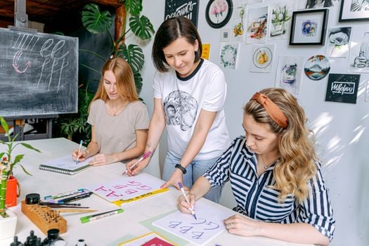 Female art instructor teaching lettering to students in a workshop.
