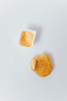 Flat lay of a crispy hash brown paired with dipping sauce on a white background.