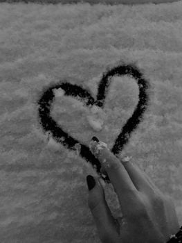 A hand draws a heart in fresh snow, capturing winter's charm.