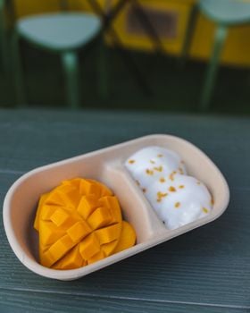 Close-up of mango sticky rice dessert with coconut cream in a compartmentalized dish on a table.