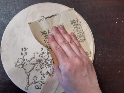 Using sandpaper to gently remove imperfections and raised fibers in the surface of the wood.