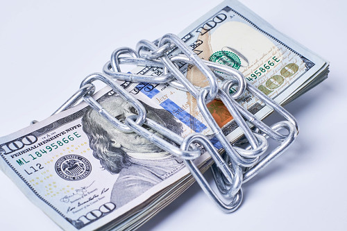 Stack of money wrapped by metal chain on white background