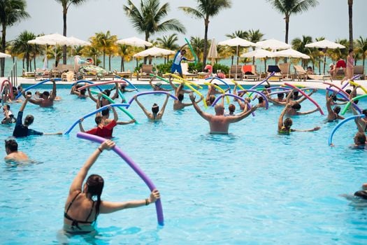 Group enjoying aqua aerobics with noodles by the pool in a tropical Cancún resort, Mexico.