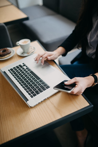 Woman working on laptop and holding smartphone in a cafe.