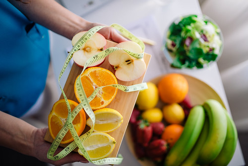 Fresh fruits with measuring tape held above a table filled with colorful healthy food choices