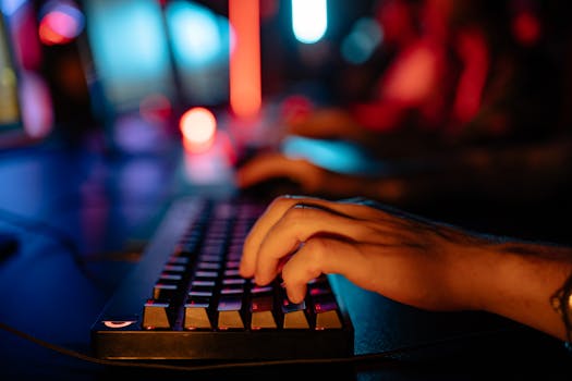 Fingers typing on an illuminated keyboard in a dimly lit room, creating a tech-focused atmosphere.