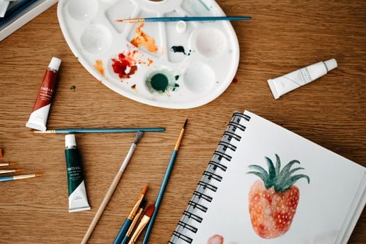 Explore a vibrant creative art space with watercolors and brushes on a wooden desk.