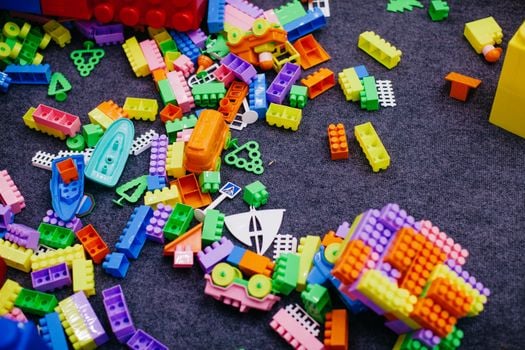 Vibrant plastic toy blocks scattered on a grey carpet, showcasing assorted shapes and colors.