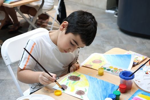 Child focused on painting at a table with colorful paints and brushes at an indoor art class.