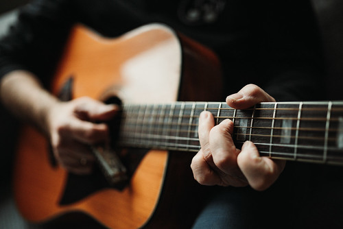 Man playing an acoustic guitar. Lef hand on guitar neck closeup.