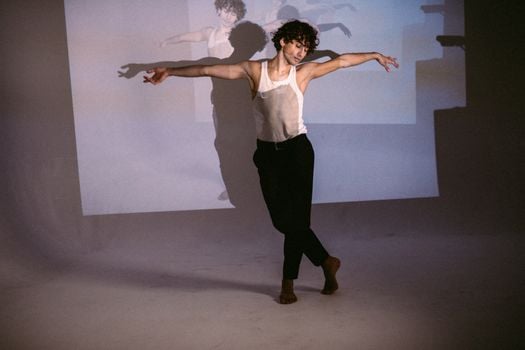 Young male ballet dancer performs gracefully in a minimalist studio setting, expressing artistic emotion.