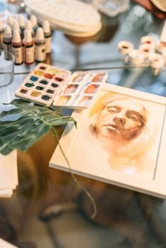 Artistic watercolor portrait with painting supplies on a glass table, showcasing craftsmanship.