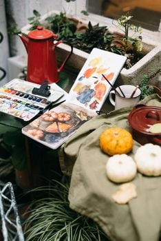 Artistic scene featuring watercolors, gourds, and a kettle in a cozy setting.