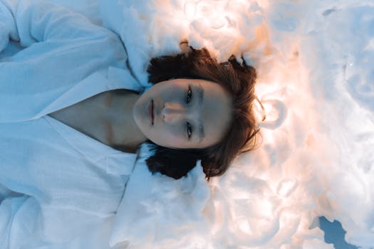 Serene portrait of an Asian woman lying on fluffy white fabric under soft lighting.