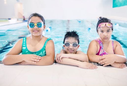 Three smiling children in swimwear enjoying a swim at an indoor pool. Perfect for lifestyle and leisure themes.