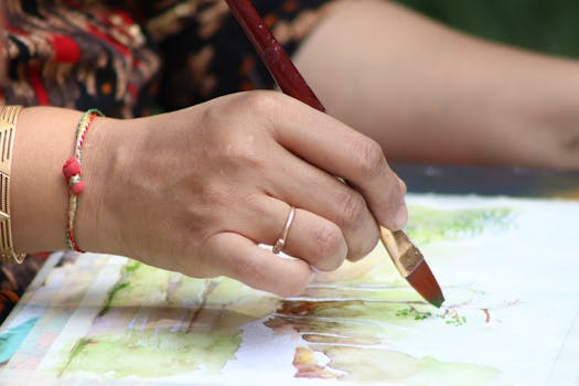 Close-up of a hand painting a watercolor outdoors, showcasing creativity and artistry.