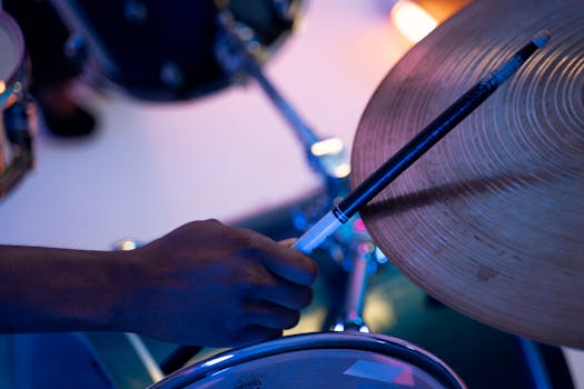 Close-up of a hand holding a drumstick striking a cymbal under blue light.