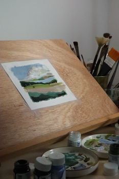 A peaceful art studio setup displaying a landscape painting on an easel with brushes and paint.