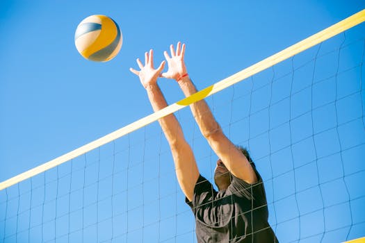 Dynamic outdoor volleyball game with a male player blocking a ball under clear blue skies.