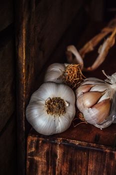A detailed close-up of fresh garlic bulbs with roots and cloves on a rustic wooden surface.