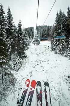 Skiers enjoy a scenic chairlift ride over a snow-blanketed alpine forest in winter.