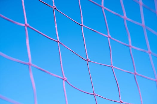 Close-up of a pink volleyball net pattern against a clear blue sky, showcasing geometric shapes.