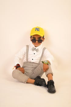 Young child in formal attire, cap, and sunglasses, studio shot.