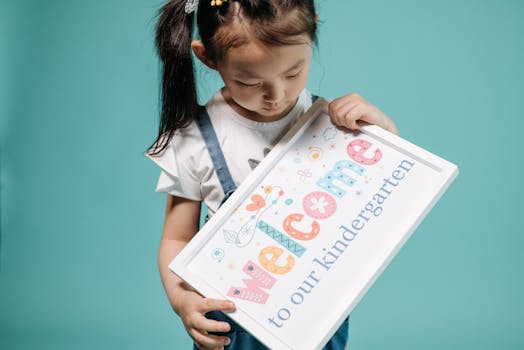 A young girl in overalls holds a colorful kindergarten welcome sign.