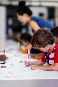 Children drawing with markers on a table during an indoor art class, fostering creativity and teamwork.