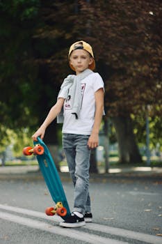 A young boy stands confidently on the street, holding a skateboard, showcasing casual style and fashion.