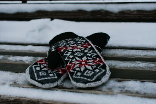 Cozy knitted mittens with a Nordic pattern rest on a snowy bench in winter.