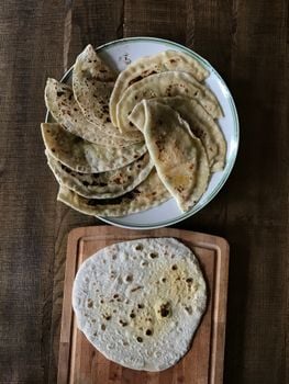 A collection of homemade ghee roti on a ceramic plate with a wooden chopping board.