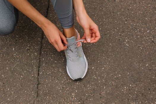 Close-up image of a person tying shoelaces on a sneaker while sitting on pavement.