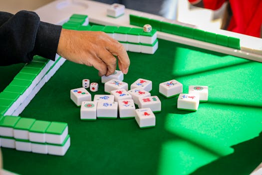 Hand arranging mahjong tiles during an intense game on a green table.