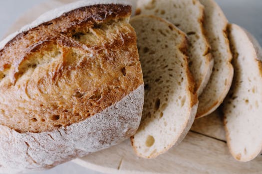 Sliced rustic bread loaf on a wooden board, showcasing fresh, golden-brown crust and soft white interior.
